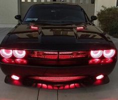 the front end of a black sports car with red lights on it's taillights