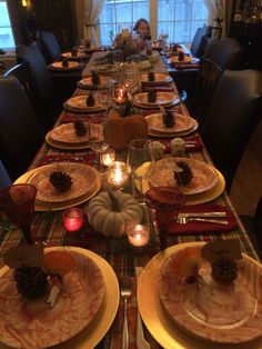 a long table set with place settings and pine cones on the plates for thanksgiving dinner