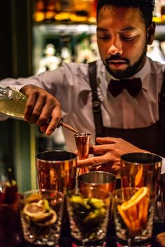 a man in an apron pours a drink at a bar with glasses on the table