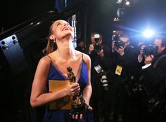 a woman holding an award in front of a group of people with cameras around her