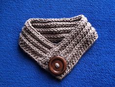 a knitted cowl with a wooden button on the end sits on a blue surface