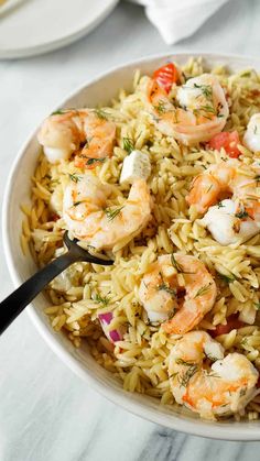 a white bowl filled with shrimp and rice on top of a marble table next to silverware