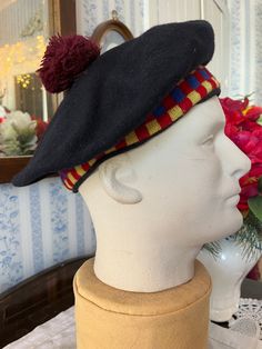 This fantastic hat is made of black wool, trimmed with a knit band in yellow, royal blue and red checks. The hat is topped with a burgundy red pom pom, and is partially lined with dark blue lining. Fits men's size medium or women's size large (the mannequin's head is 21 inches around). In very good condition. Retro Black Beret For Winter, Hat With Pom Pom, Blue Yellow Red, Mannequin Heads, Beret Hat, Pom Pom Hat, Black Hat, Burgundy Red, Black Wool