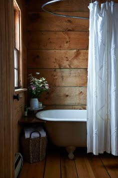 a bath tub sitting next to a shower curtain in a room with wooden walls and flooring