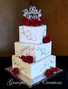 a three tiered white wedding cake with red roses on the side and diamond decorations