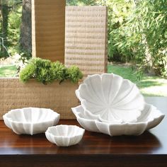 three white bowls sitting on top of a wooden table next to a planter and window