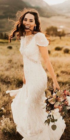 a woman in a white dress holding a bouquet and smiling at the camera while standing in a field