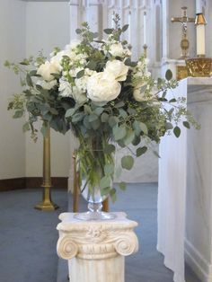 a vase filled with white flowers sitting on top of a table next to a pillar