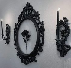 two black candles are lit in front of a mirror and wall with an ornate frame