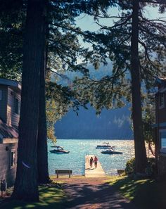 two boats are docked at the end of a dock in front of some houses and trees