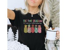 a woman is holding a cup and wearing a t - shirt that says tis the season