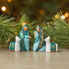 three nativity figurines sitting on top of a table next to pine branches