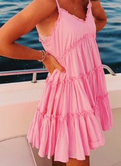 a woman in a pink dress standing on a boat with her hands on her hips