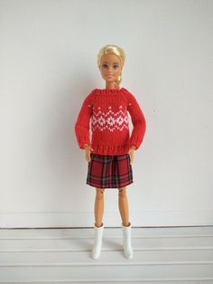 a barbie doll wearing a red sweater and plaid skirt with white boots, standing in front of a white wall