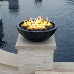 an outdoor fire pit sitting on top of a cement block near the water's edge