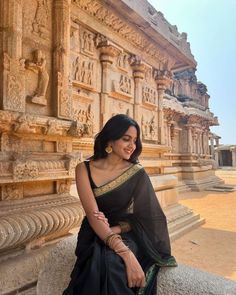 a woman sitting on top of a stone wall next to a tall building with carvings