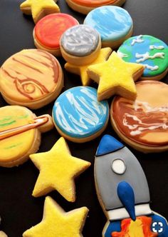 cookies decorated with different designs and colors on a black surface, including one rocket ship