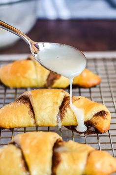 a spoon drizzling sauce onto pastries on a cooling rack