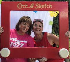 two women in pink shirts are standing behind a red frame with the words etch and sketch on it