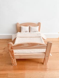 a wooden bed with two pillows on top of it in a white room next to a wood floor