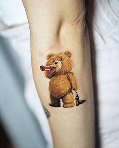 a tattoo with a teddy bear holding a wine bottle on it's left arm