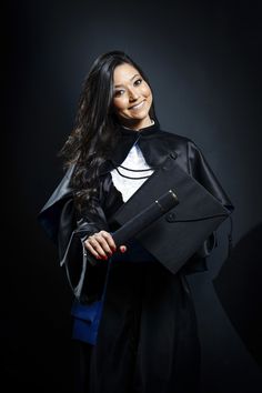 a woman dressed in black holding a purse and smiling at the camera while standing against a dark background