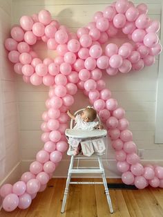 a baby in a highchair surrounded by pink balloons that spell out the letter k