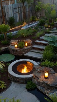 an outdoor fire pit surrounded by plants and rocks with lit candles in the center on either side