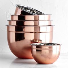 a stack of copper colored pots sitting on top of a white counter next to each other