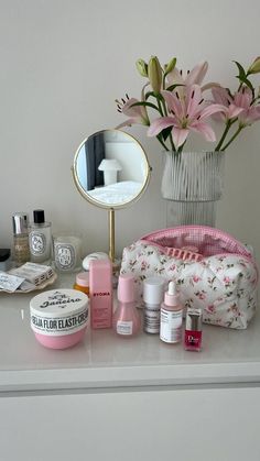 a white dresser topped with lots of beauty products next to a vase filled with flowers