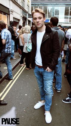 a young man standing in the middle of a street with people walking around and onlookers