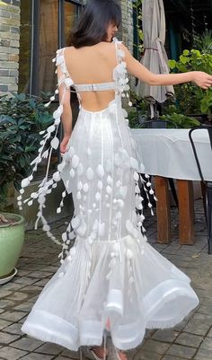 a woman in a white dress standing on a brick patio with her back to the camera