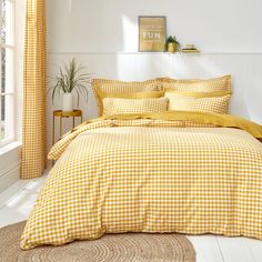 a yellow and white checkered comforter set with pillows on the bed in front of a window