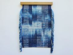 a blue and white wall hanging with fringes on it's side next to a wooden frame