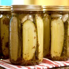 four jars filled with pickles sitting on top of a red and white towel next to each other