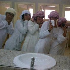 four men in white robes taking pictures with their cell phones while standing in front of a bathroom mirror