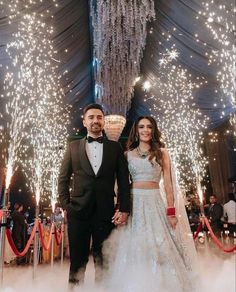 two people in formal wear standing next to each other under a chandelier filled with lights