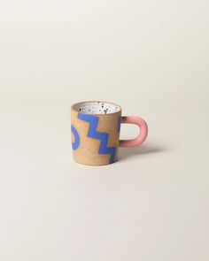 a coffee cup with blue and pink handles sitting on a white surface, in front of a plain background