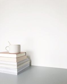 a stack of books with a coffee cup on top of it next to a white wall