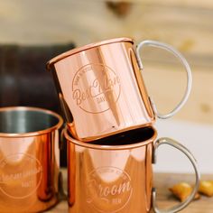 three copper colored coffee mugs sitting on top of a wooden table next to each other