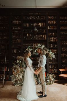 a bride and groom standing in front of a bookshelf with flowers on it