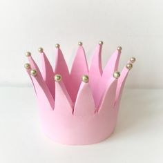 a pink paper crown with gold beads on it's sides, sitting on a white surface