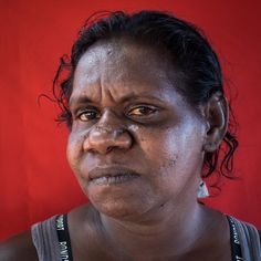 a woman with wrinkles on her face looks at the camera while standing in front of a red wall