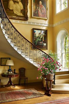 a staircase with paintings on the wall and flowers in a pot next to it,