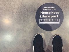 a pair of shoes standing in front of a sign that says please keep 1 5m apart