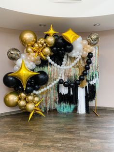 black, gold and white balloons in the shape of stars are hanging on a wall