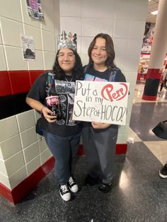 two women standing next to each other holding signs