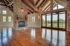 an empty living room with wood flooring and stone fireplace in the center surrounded by large windows