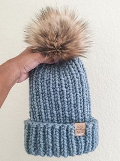 a hand holding a blue knitted hat with a brown pom - pom