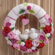 a crocheted wreath with two white doves and roses on it, hanging from a wooden wall